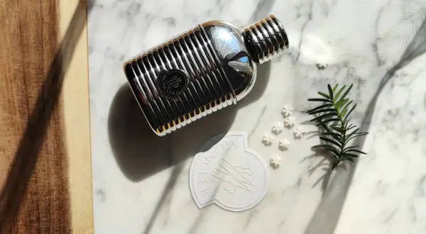 Elegancki flakon perfum Moncler pour homme na marmurowym tle, otoczony gałązką iglaków i płatkami śniegu.