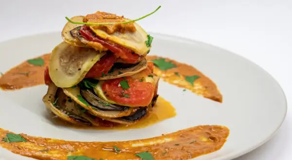 Ein gestapeltes Ratatouille-Rezept auf einem Teller, garniert mit Sauce und Kräutern.