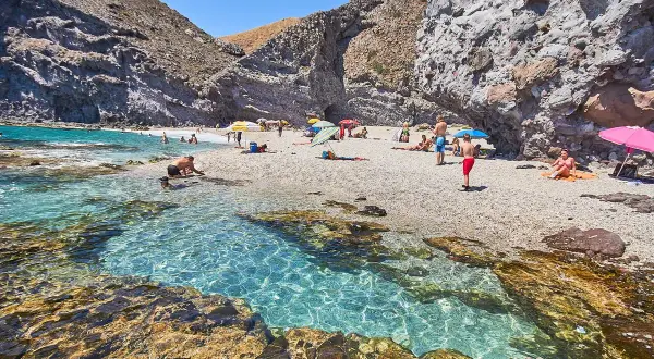 Descubre qué ver en Carboneras: una cala rocosa con aguas cristalinas y gente disfrutando del sol y el mar.