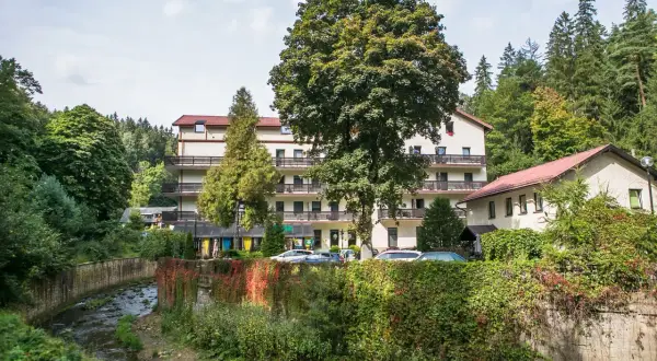 Sanatorium uzdrowiskowe Malwa otoczone zielenią, z potokiem i drzewami.