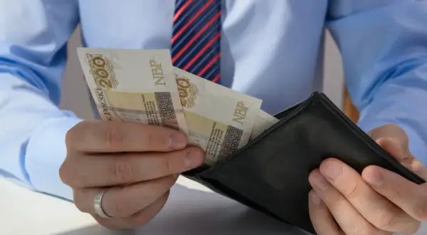 Mężczyzna w koszuli i krawacie wkłada polskie banknoty 200 zł do czarnego portfela.