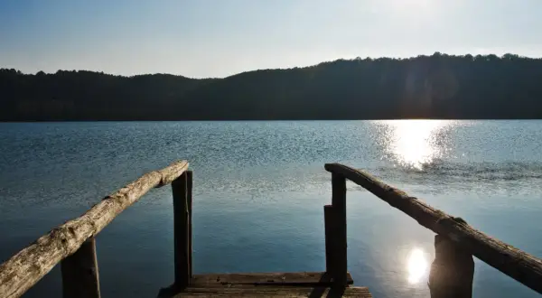 Un pontile in legno si affaccia sul lago di Mezzano, con il sole che brilla sull'acqua e le colline sullo sfondo.