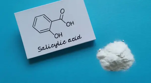 Kwas salicylowy na twarz: biały proszek i jego wzór chemiczny na kartce.