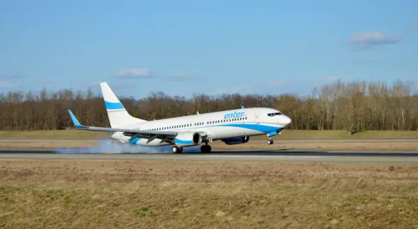 Samolot Enter Air ląduje, koła dotykają pasa, unosząc pył.