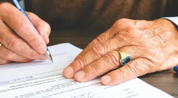 Dłoń z sygnetem podpisuje dokument. Ważne jest skierowanie na badania, aby uzyskać właściwą diagnozę.