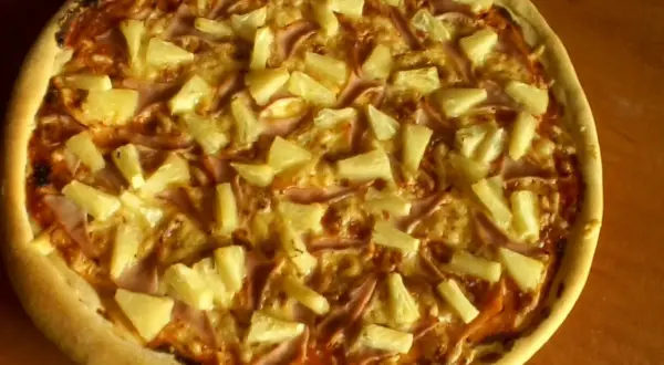 Pyszna pizza z ananasem i szynką, zrumieniona skórka i złocisty ser.