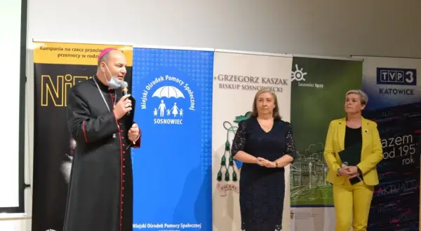 Biskup sosnowiecki przemawia na tle banerów kampanii przeciw przemocy w rodzinie i MOPS Sosnowiec.