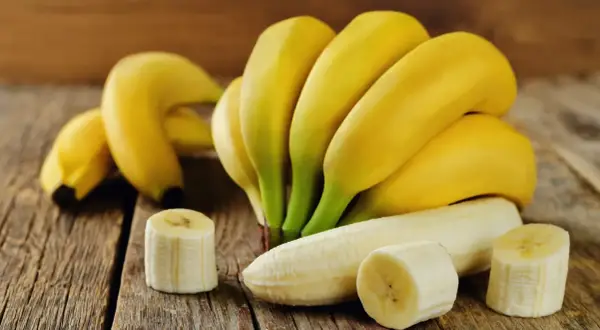 Kilka dojrzałych bananów, jeden obrany i pokrojony, na drewnianym blacie. Zastanawiasz się, ile cukru ma banan?