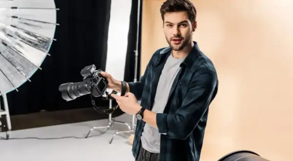 Młody fotograf z aparatem w studio. Świetna robota!
