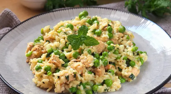 Pyszne risotto z groszkiem i kawałkami kurczaka, udekorowane listkiem mięty. Idealne na lekki obiad.