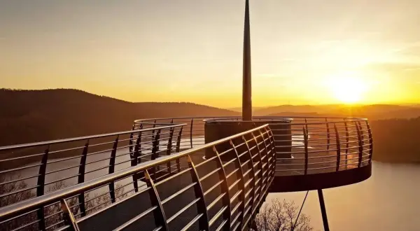 Ein Skywalk NRW bei Sonnenuntergang mit Blick auf einen See und bewaldete Hügel.