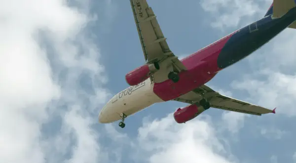 Samolot Wizz Air z wysuniętym podwoziem na tle nieba z chmurami.