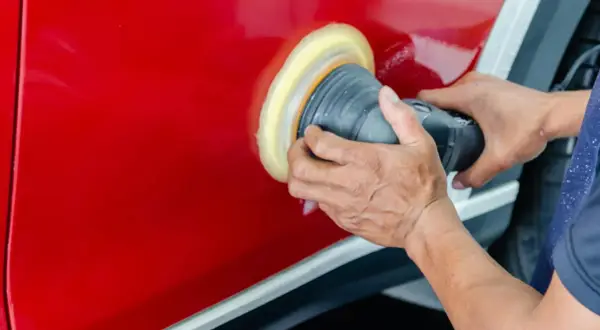 Ręce polerują czerwony lakier auta maszyną polerską. To kluczowy etap, jak woskować auto, by uzyskać lustrzany połysk i ochronę.