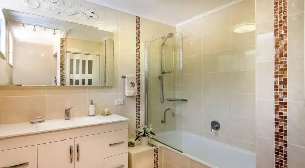 Baño moderno con ducha y bañera, lavabo con mueble y espejo decorado con un lagarto. El alicatar baño resalta con detalles en mosaico.