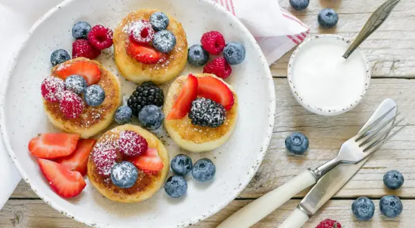 Deliziosi pancake senza glutine guarniti con fragole, lamponi, mirtilli e more. Serviti con yogurt e spolverata di zucchero a velo.
