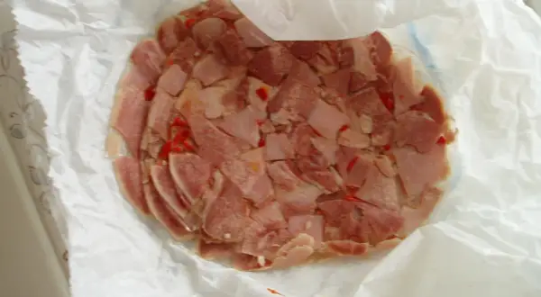 Rebanadas de queso de cabeza con trozos de pimiento rojo, envueltas en papel blanco.
