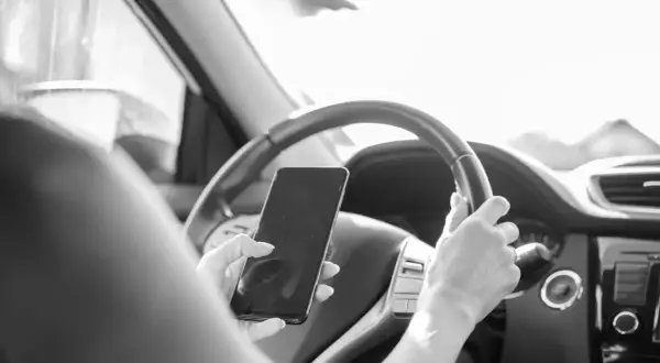 Une main tient un téléphone au volant, distrayant le conducteur. Une conduite dangereuse qui peut coûter 6 points sur le permis.