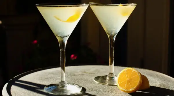 Dwa drinki z wódką waniliową i cytryną, podane w kieliszkach martini na kamiennym stoliku.