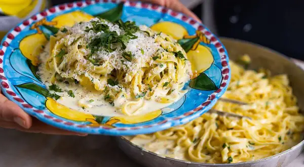 En tallrik med krämig pasta al limone, toppad med parmesan och persilja, serveras från en panna.