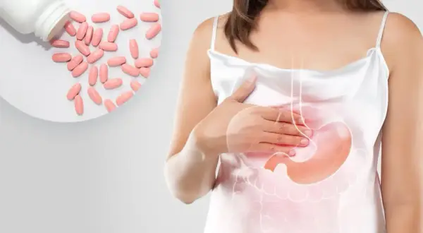 Kobieta z bólem brzucha, obok tabletki. Leki z grupy inhibitory pompy protonowej pomagają złagodzić dolegliwości.