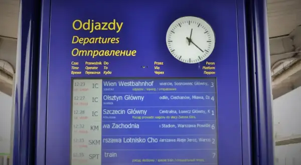 Tablica odjazdów PKP z zegarem. Widoczne pociągi do Wiednia, Olsztyna, Szczecina, Warszawy Zachodniej i innych. Kiedy zmiana rozkładu jazdy PKP, warto sprawdzić tablicę.