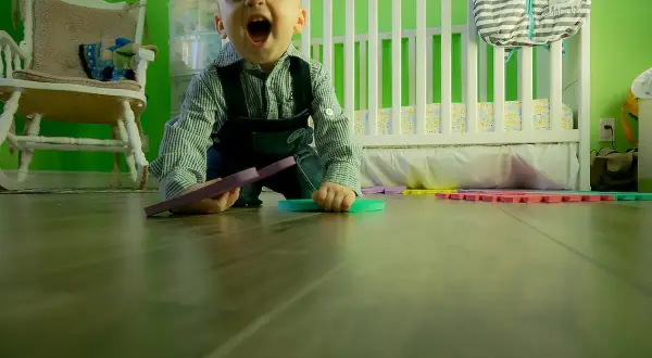 Wesołe dziecko kiedy dziecko raczkuje, bawi się kolorowymi puzzlami na podłodze w pokoju dziecięcym.