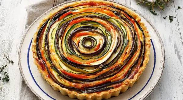 Quiche de verduras con hojaldre, un remolino de calabacín, berenjena y tomate sobre una base dorada.