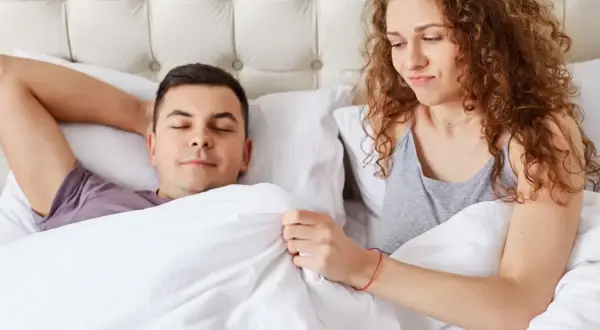 Kobieta z zaciekawieniem patrzy na śpiącego mężczyznę, zastanawiając się, dlaczego penis staje.