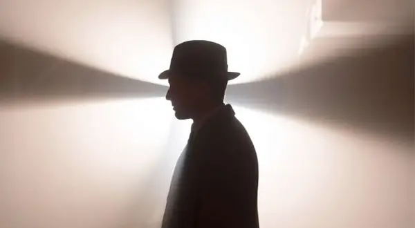Ein Mann im Hut und Anzug, im Profil, vor einem hellen, strahlenden Hintergrund. Ein mysteriöser Blick, der an Babylon Berlin Staffel 5 erinnert.