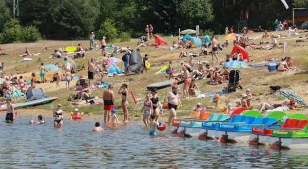 Tłum ludzi wypoczywa na plaży nad jeziorem Nakło Chechło. Woda jest spokojna, a na brzegu widać kolorowe rowerki wodne.