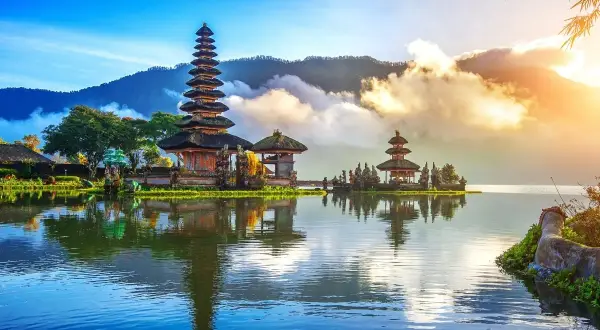 Świątynia Pura Ulun Danu Bratan na Bali, odbijająca się w spokojnej tafli jeziora, otoczona górami i chmurami.