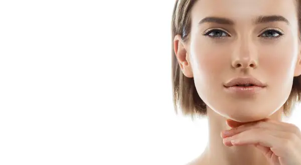 Primo piano di una donna con pelle luminosa e un tocco sul mento, un'ispirazione per chi cerca come snellire il viso con un look naturale.