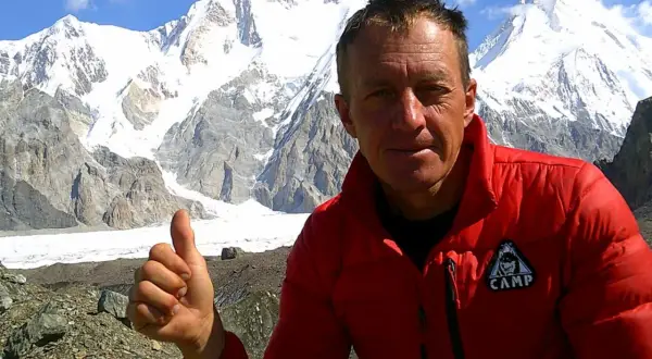 Bergsteiger Denis Urubko gibt Daumen hoch vor schneebedeckten Gipfeln.