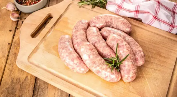 Surowa biała kiełbasa na desce, gotowa do przygotowania. Zioła i przyprawy dodają apetycznego wyglądu.