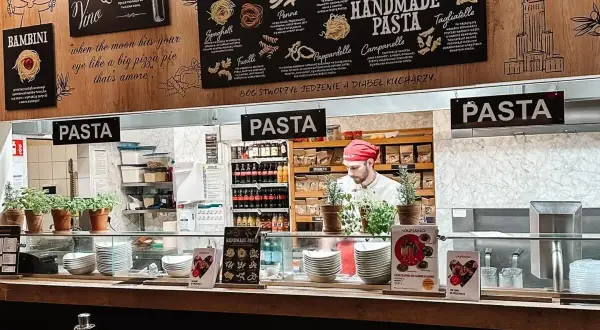 W Vapiano kucharz przygotowuje ręcznie robiony makaron. Na ścianie menu z różnymi rodzajami pasty.