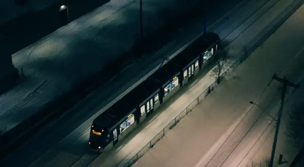 Pociąg Warszawskiej Kolei Dojazdowej mija ośnieżone tereny nocą.