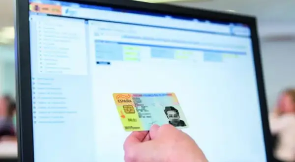 Mano sostiene DNI español frente a pantalla de ordenador con interfaz de gestión. Apoderamiento DGT.