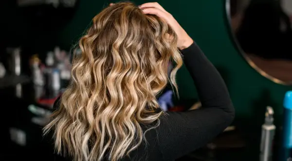 Blond włosy z pięknymi falami, podkreślonymi przez aktywator skrętu włosów. W tle widać kosmetyki fryzjerskie.