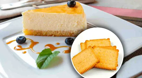 Una fetta di cheesecake con topping giallo, mirtilli e salsa caramello, accompagnata da biscotti secchi. Diversi tipi di cheesecake per ogni gusto.