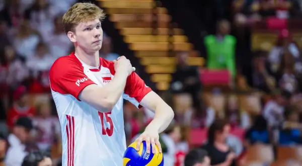 Młody siatkarz Jakub Kochanowski, numer 15, w biało-czerwonej koszulce reprezentacji Polski, z piłką w dłoni. Jego wzrost robi wrażenie.