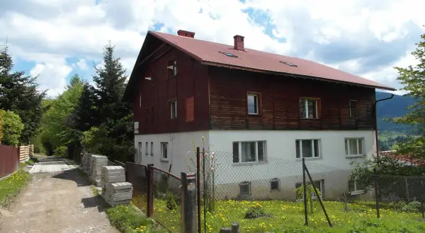 Stacja turystyczna Abrahamów, drewniano-betonowy budynek z czerwoną dachem, otoczony zielenią i polnymi kwiatami.