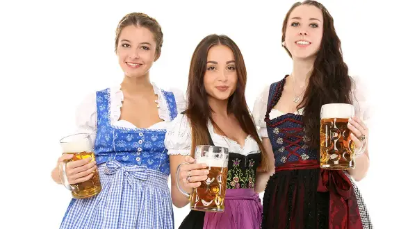 Trzy uśmiechnięte kobiety w tradycyjnych strojach dirndl, trzymające kufle piwa.