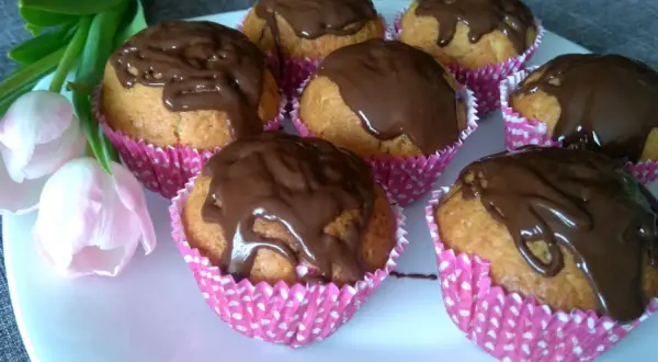 Pyszne muffiny z powidłami śliwkowymi, polane czekoladą, na talerzu z tulipanami.