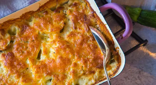 Goldbraun überbackener Kartoffel Zucchini Auflauf in einer Auflaufform, bereit zum Servieren.