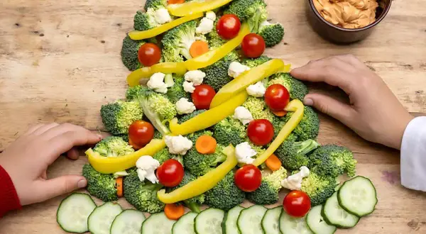 Une joyeuse planche apéritif noël en forme de sapin, décorée de brocolis, tomates cerises, poivrons jaunes, chou-fleur et rondelles de concombre.