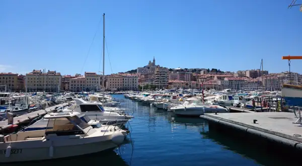 Widok na port w Marsylii z wieloma łodziami i budynkami w tle.