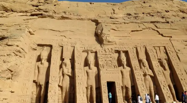 Gigantescas estatuas talladas en la roca flanquean la entrada del templo de Abu Simbel. Turistas admiran la majestuosidad de este sitio histórico.