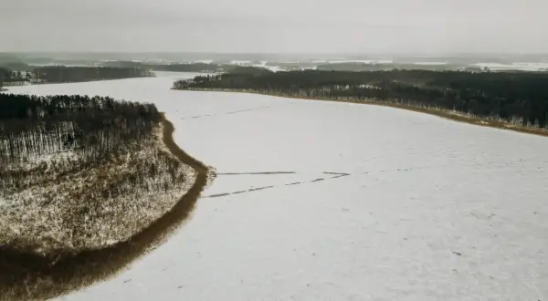 Zimowy krajobraz: zamarznięte jezioro Tyrkło otoczone lasem. Śnieg pokrywa taflę wody, tworząc białą, rozległą przestrzeń.