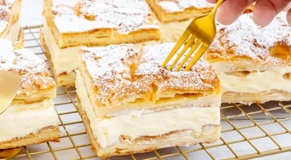 Ein goldener Löffel sticht in ein Stück polnischer Puddingkuchen, bestäubt mit Puderzucker.