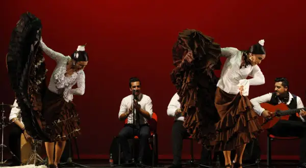 Bailarinas de flamenco con volantes, guitarrista y percusionista. La pasión del flamenco, su saeta significado, cobra vida en el escenario.